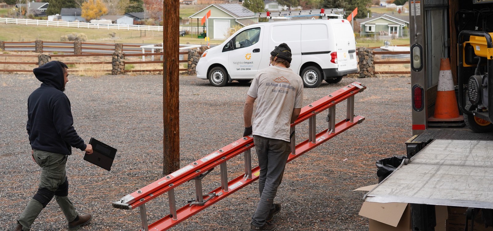 Two workers carry a ladder beside a NeighborImpact vehicle.